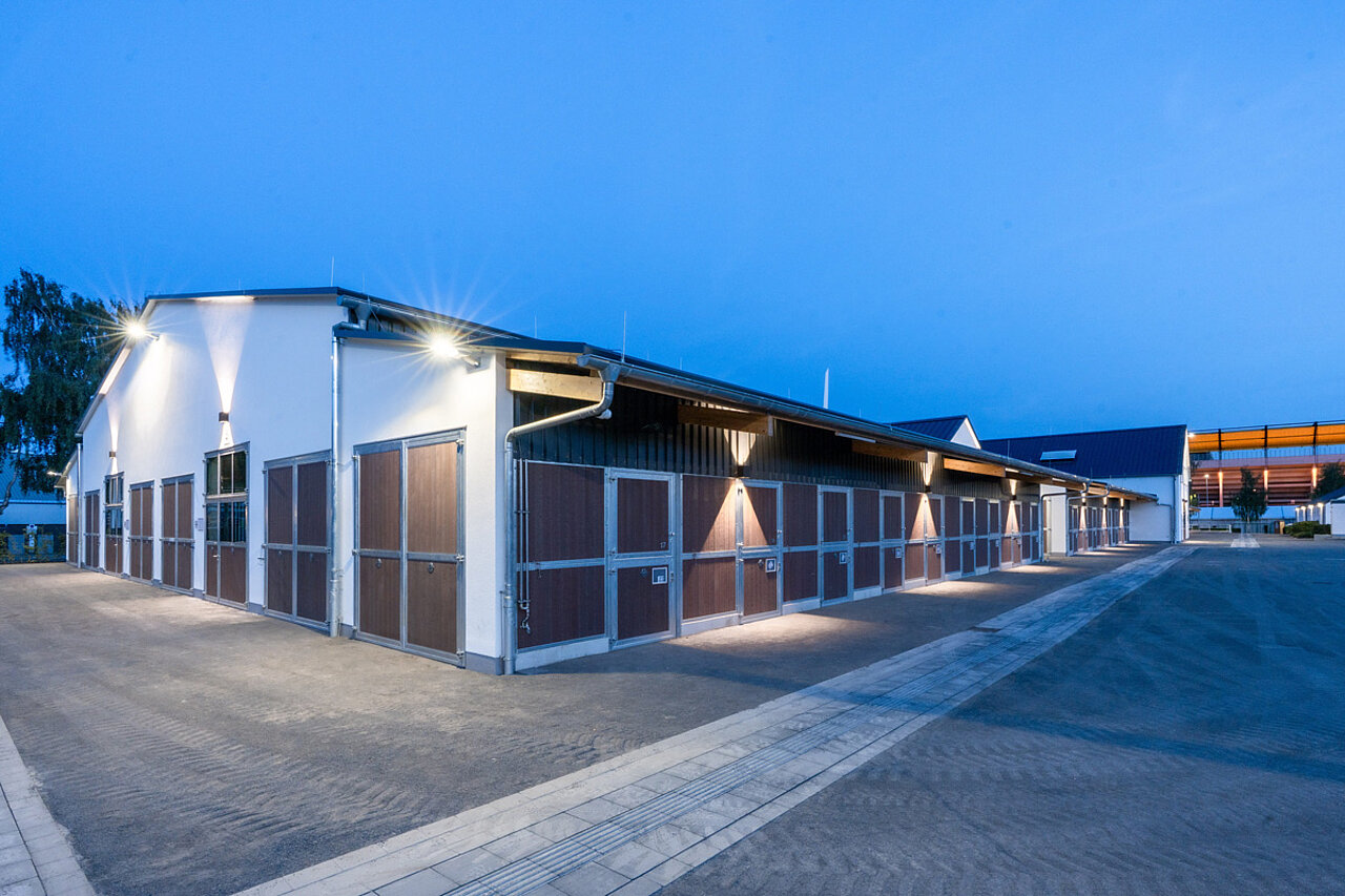 Beleuchtete Außenboxen des neuen Stallgebäudes bei einsetzender Dämmerung