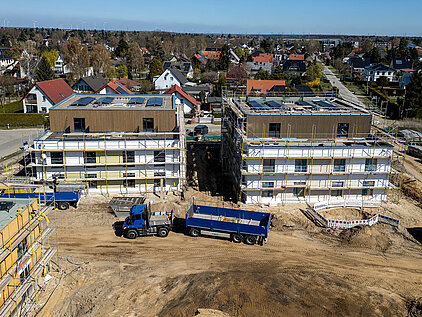 Zwei Mehrfamilienhäuser in Holz-Hybrid-Bauweise mit Fassadenarbeiten, Gerüst und Baustellenfahrzeug