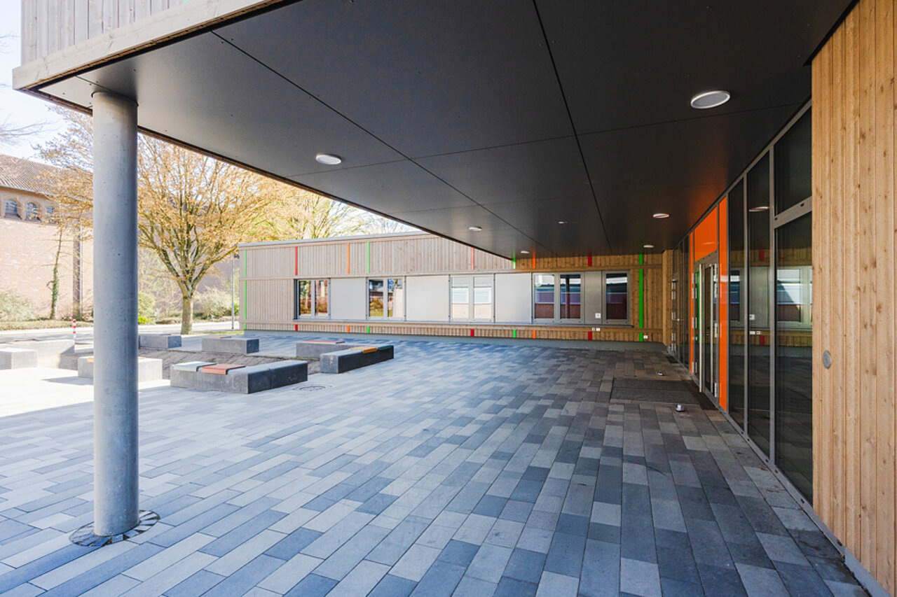 Überdachter Schulhofbereich mit Holzfassade und Pflasterfläche