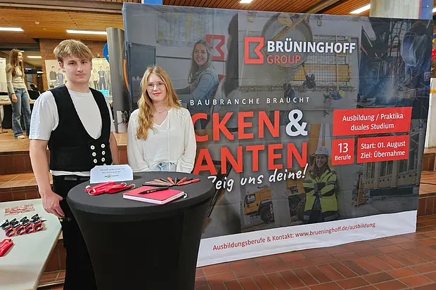 Zwei Auszubildende der Brüninghoff Group stehen vor einem Messestand einer Ausbildungsmesse